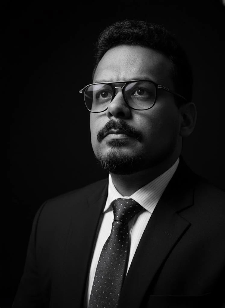 Retrato autoral em preto e branco de Thiago Andrade usando óculos.